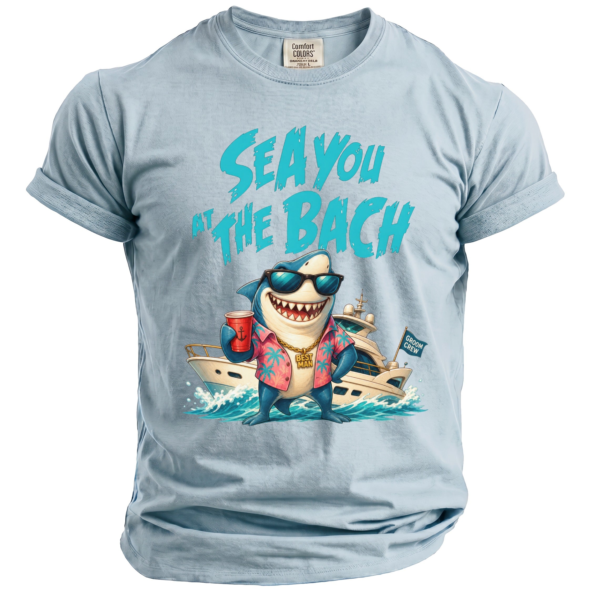 Light blue t-shirt featuring a graphic of a shark wearing sunglasses, a floral shirt, and a gold chain, standing in front of a yacht with the text "SEA YOU AT THE BACH".