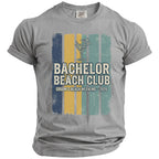 Grey t-shirt with "Bachelor Beach Club" and "Groom's Beach Weekend - 2026" text.