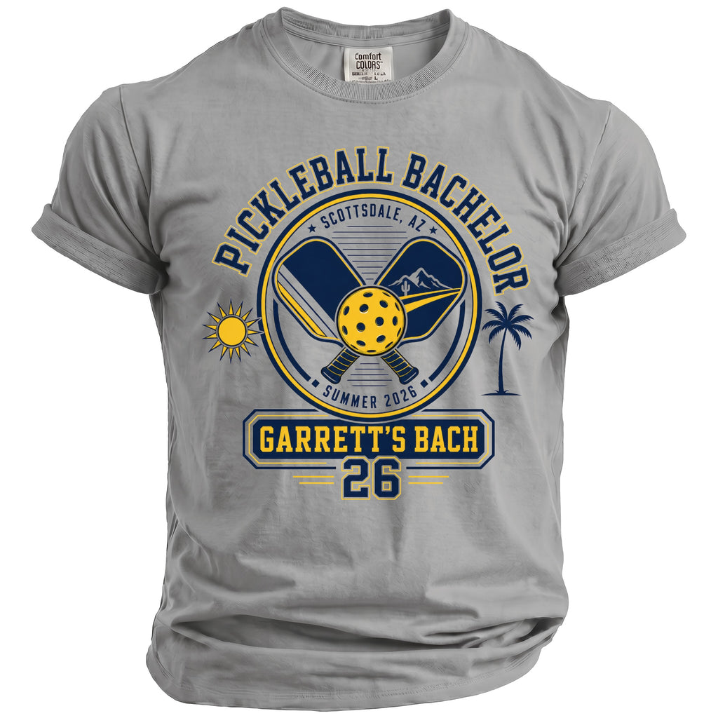 Gray t-shirt with "Pickleball Bachelor" graphic including paddles, ball, sun, mountain, and palm.