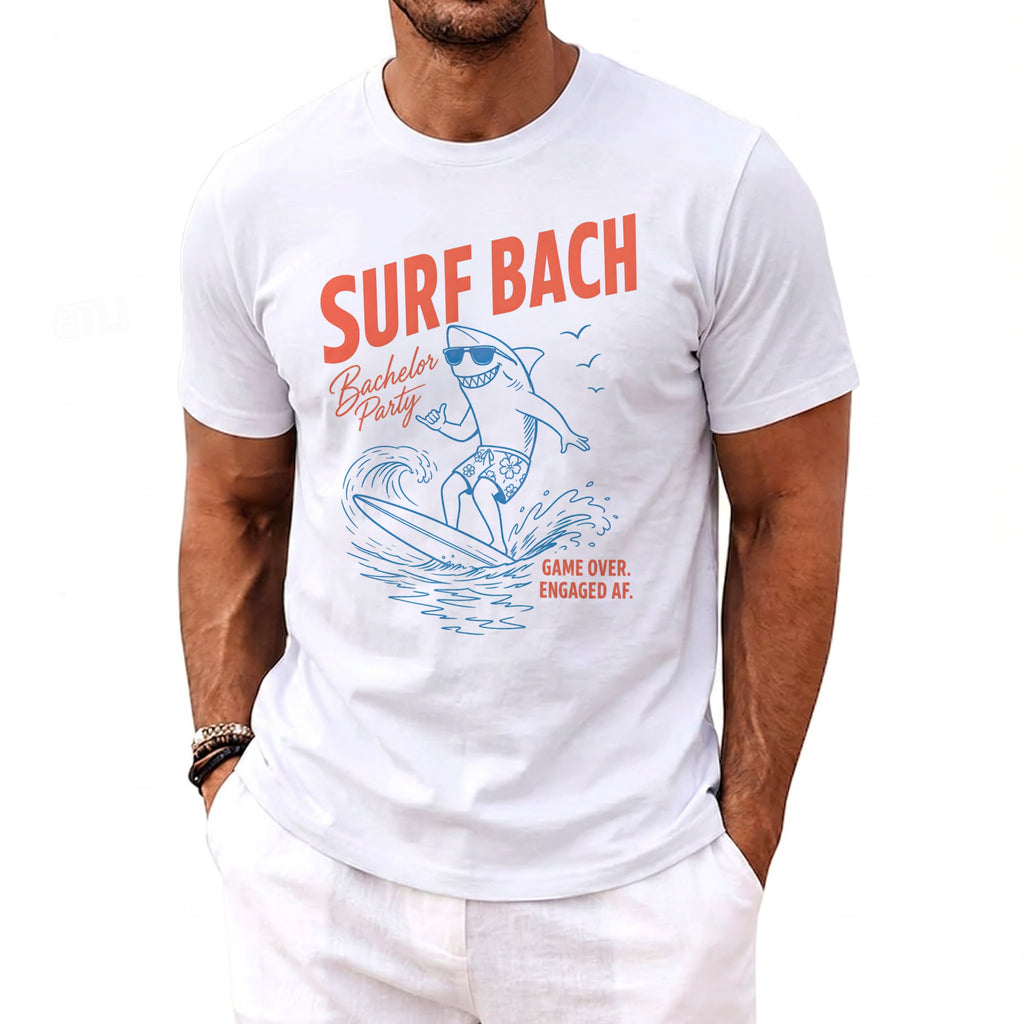 White t-shirt with "Surf Bach" text and a surfing shark graphic.
