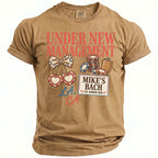Tan Comfort Colors t-shirt with "Under New Management," cherries, and "Mike's Bach" text.