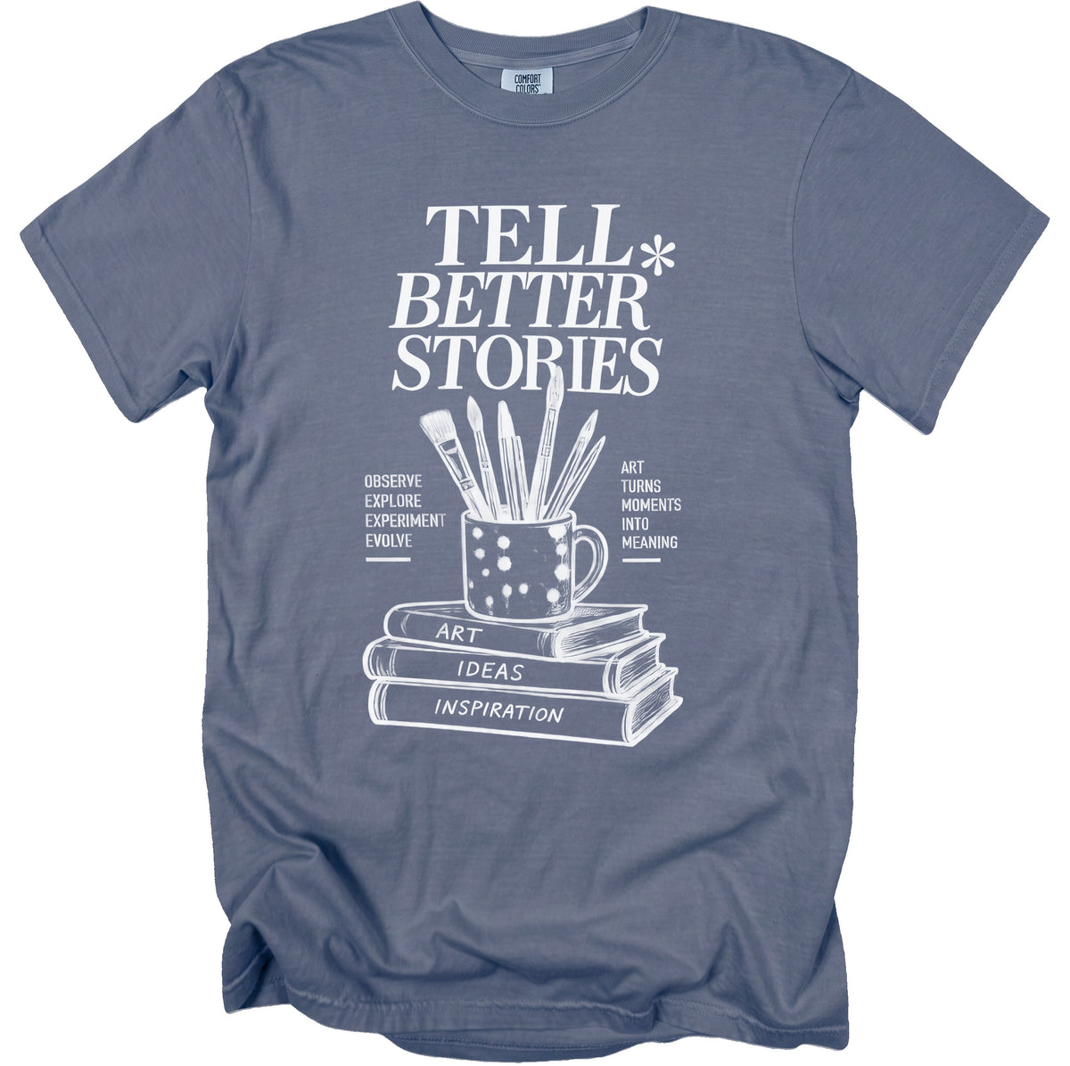 T-shirt with "Tell Better Stories" and art supplies over books.