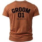 Brown t-shirt with black text "GROOM 01 [NAME] - BACH 2026 - [CITY]"