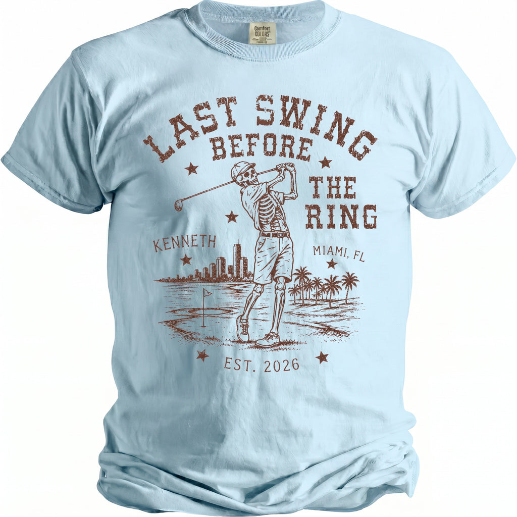 Light blue t-shirt with brown graphic: Skeleton golfing, "Last Swing Before The Ring," Kenneth, Miami, FL, Est. 2026