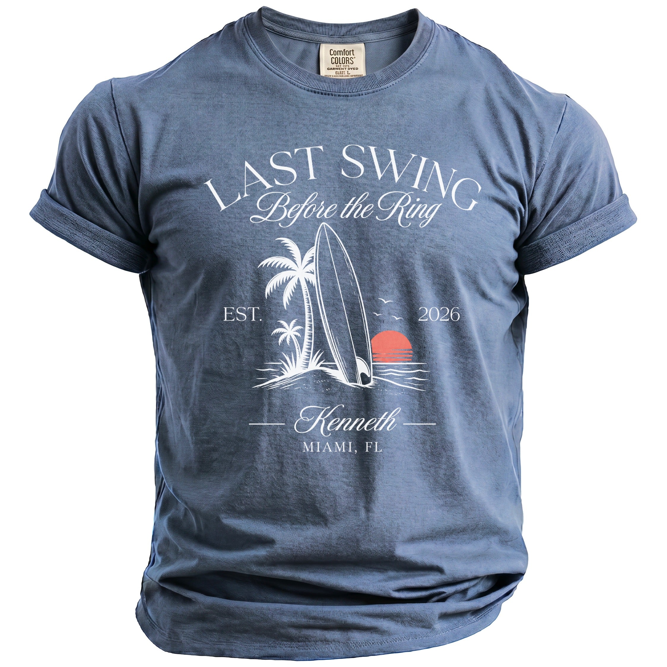 Blue t-shirt with "Last Swing Before the Ring" graphic, surfboard, palm trees, and sunset.