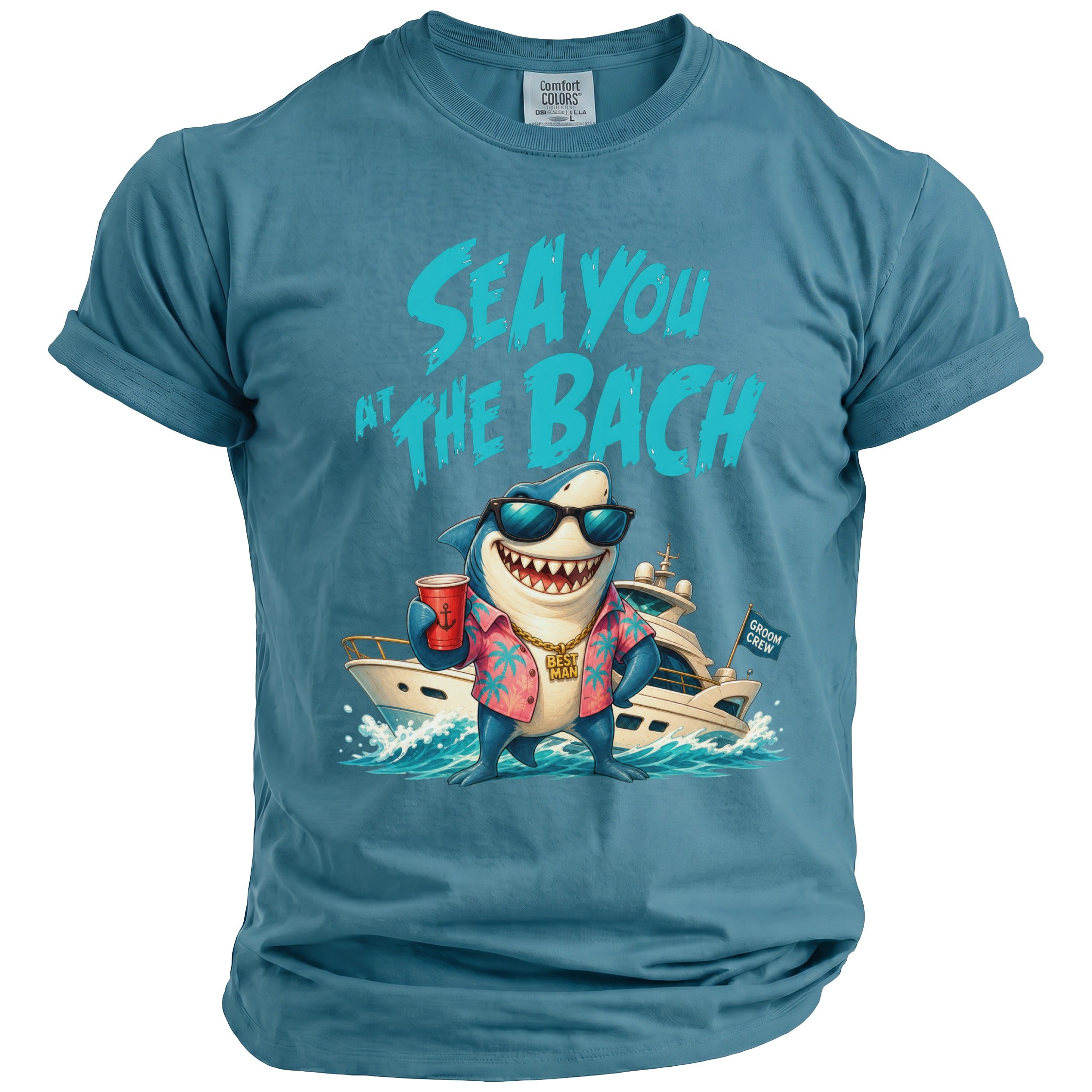 A blue t-shirt featuring a graphic of a shark wearing sunglasses, a floral shirt, and a gold chain, standing on a yacht in front of the text "SEA YOU AT THE BACH".