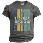 Dark gray t-shirt with "Bachelor Beach Club Groom's Beach Weekend 2026" graphic.